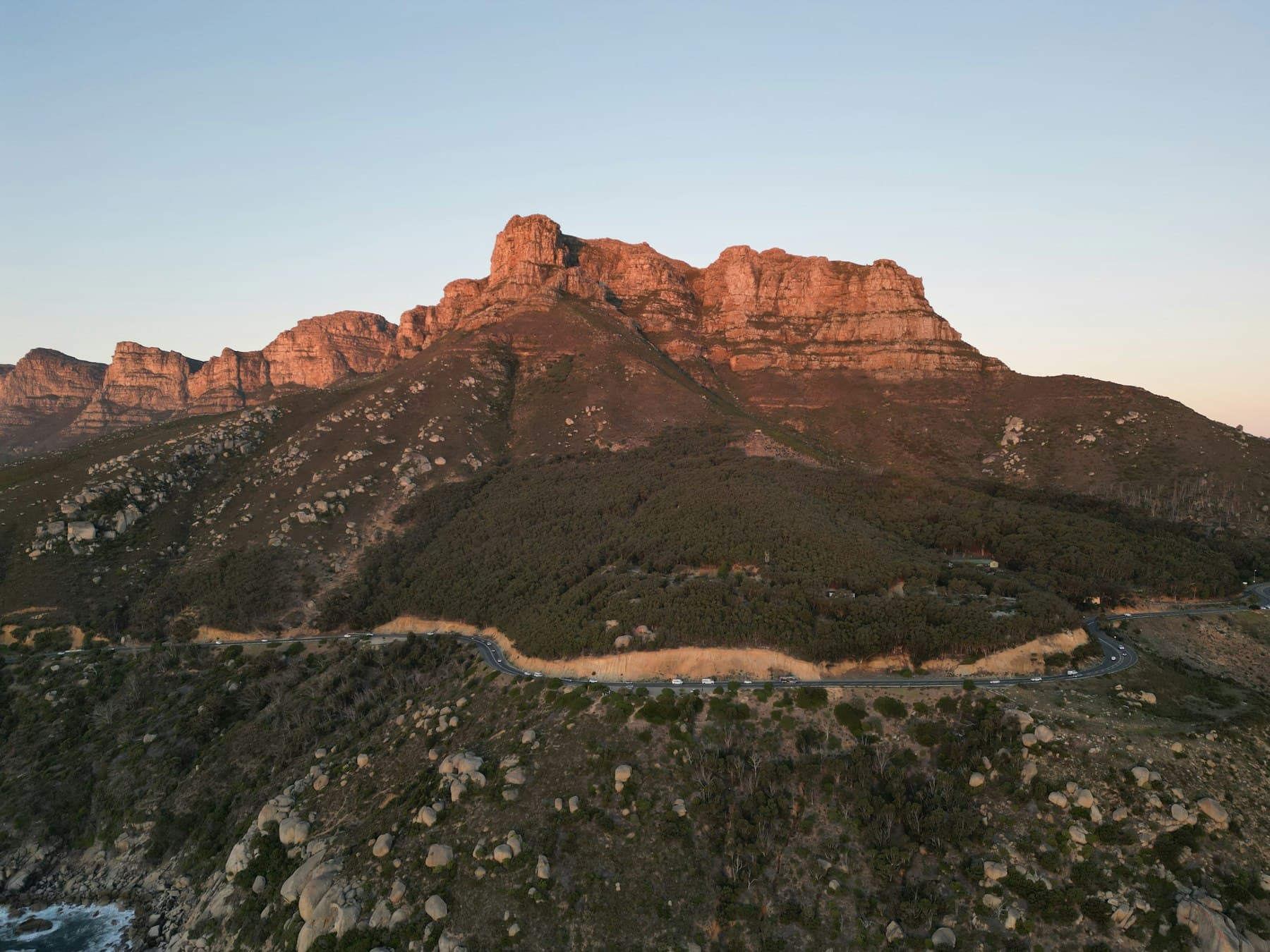 Stock placeholder: a sandstone mountain range at golden hour above a coastal road near Cape Town.